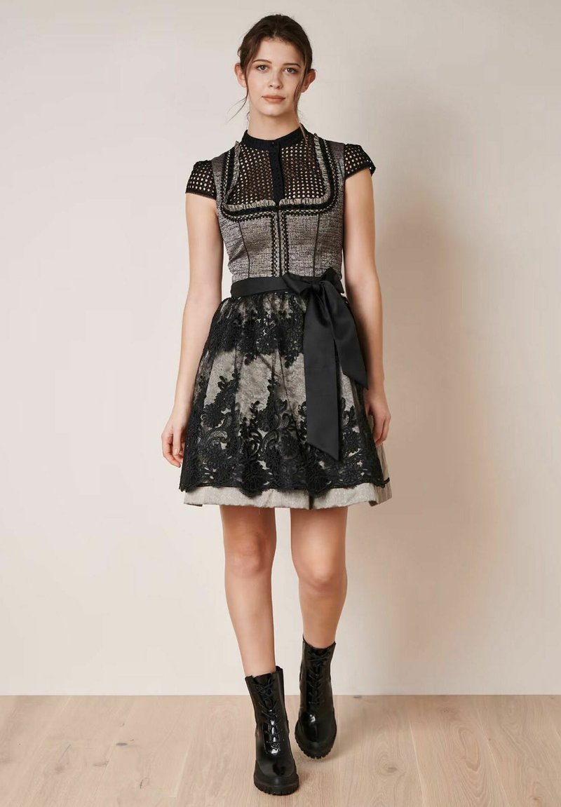 Schwarz-graues Kleid mit einem strukturierten, figurbetonten Oberteil, Spitzenakzenten am Rock und einem satinierten Gürtel in der Taille, kombiniert mit glänzenden schwarzen Stiefeln.