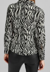 Black and white zebra-patterned shirt with long sleeves, a collar, and buttoned cuffs, made from a textured fabric, paired with black pants.