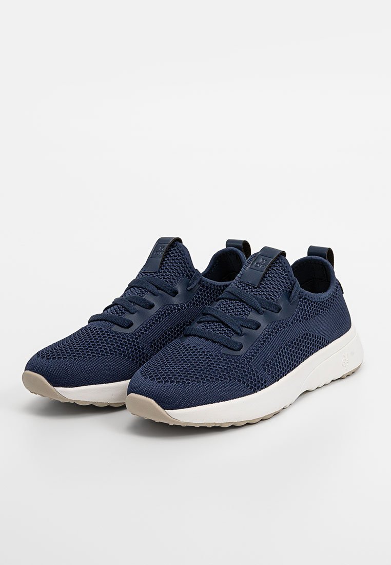 Granatowe buty sportowe z oddychającej siateczki, wydłużony kształt, zaokrąglony czubek i biała gumowa podeszwa. Posiadają sześć pętli na sznurówki.