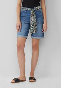 Shorts de mezclilla con un cinturón estampado, que presentan un corte ajustado, dobladillos enrollados y un lavado azul claro. Chanclas negras con un detalle de hebilla.