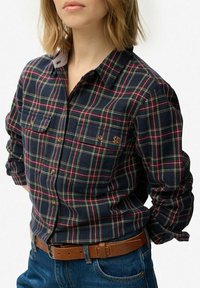 Navy plaid flannel shirt with red and green accents, button-up front, two chest pockets, and a logo on the left pocket.