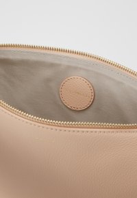 Hnědo-oranžová kožená taška s texturovaným povrchem a zlatým zipem. Interiér je vybaven béžovou látkovou podšívkou a kulatým koženým štítkem s embosovaným textem.