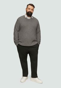 Grau strukturierter Pullover mit Rauten-Muster, weißes Hemd mit Kragen darunter, schwarze Hose und weiße Sneaker. Legere Outfit-Präsentation.