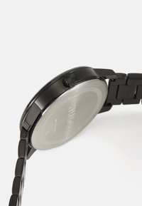 Reloj de acero inoxidable negro con una caja redonda, corona texturizada negra y pulsera de eslabones. Presenta un fondo de caja grabado en tono plateado.