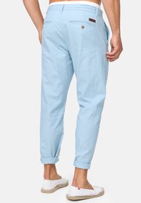 Pantaloni di lino azzurro chiaro con una vestibilità rilassata, dotati di una tasca posteriore con chiusura a bottone e risvolti. Indossati con scarpe bianche senza lacci.