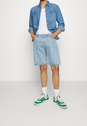 Shorts en denim de couleur bleu clair avec un ourlet effiloché, associés à une chemise en denim à boutons et des baskets colorées avec des accents verts, blancs et violets.