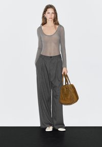 Light gray sheer long-sleeve top paired with charcoal pinstriped wide-leg trousers; model holds a brown suede handbag. White slip-on shoes.