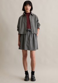 Siva jakna sa prugicama preko maroon rebrastog topa i sive suknje, naglašena crnim pojasom. Uparena s crnim masivnim obuvama i čarapama.