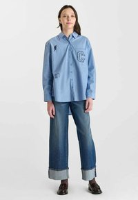 Blue striped button-up shirt with embroidered details and a relaxed fit, paired with wide-leg denim pants featuring contrasting cuffs.