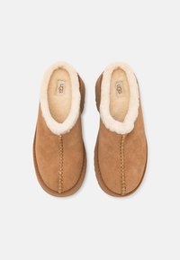 Paire de chaussons UGG en daim beige avec doublure polaire blanche et surpiqûres apparentes, vue de dessus sur fond blanc.