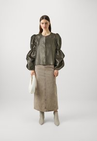 Blusa verde metallica con texture e maniche a sbuffo, abbinata a una gonna di denim beige. Stivaletti grigi alla caviglia e una borsa bianca completano il look.