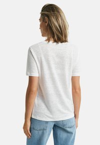 Weißes Kurzarm-T-Shirt aus strukturiertem Stoff mit rundem Ausschnitt. Getragen mit hellblauen Denim-Jeans.