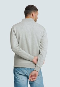 Grijze sweatshirt met een kraag, lange mouwen en textuurstof. Draagt met een blauwe spijkerbroek, van achteren bekeken, met een eenvoudig ontwerp.