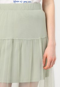 Jupe stratifiée vert clair en tulle avec une texture douce et transparente, ornée d'accents froncés, dotée d'une taille élastique.