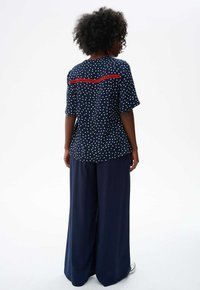 Marineblauw polka dot top met rode afwerking, gecombineerd met brede marineblauwe broek. Stof lijkt zacht; ontwerp heeft korte mouwen en een losse pasvorm.