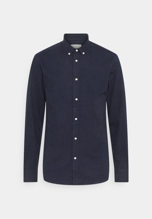 Chemise bleu marine à manches longues de style boutonné, confectionnée dans un tissu texturé avec des boutons blancs en accent le long de la patte de boutonnage frontale.