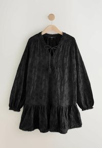 Robe noire brodée avec des manches longues, décolleté rond et accent de cordon. Présente un ourlet à volants et des motifs floraux tout au long.