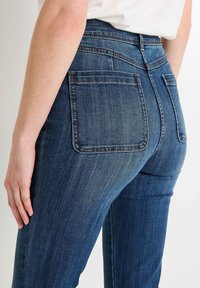 Jeans de mezclilla azul oscuro con un diseño de cintura alta, que presentan bolsillos traseros y un leve efecto de desgaste. La textura parece suave con costuras sutiles.
