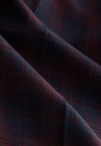 Tissu foncé avec un subtil motif à carreaux dans des nuances de rouge profond, bleu marine et vert, présenté avec des plis doux et un détail de tissage texturé.