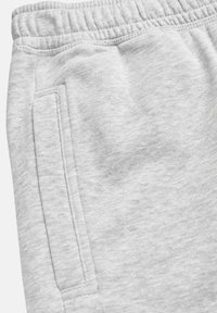 Close-up van lichtgrijze joggingbroekstof met details van het zijzakje en de stiknaden van de elastische tailleband.