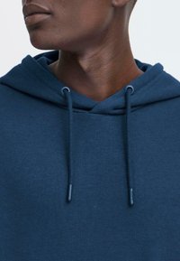 Felpa blu navy realizzata in materiale morbido, con cappuccio regolabile, texture a coste e design minimalista privo di motivi o loghi.