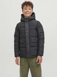 Black puffer jacket with a hood, featuring a vertical logo stripe, two front pockets, and elastic cuffs. Worn with olive green pants.