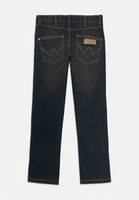 Mörkblå denimjeans med rak bendesign. Har snörliknande gul sömnad på bakfickorna och en tan läderlapp vid midjan.