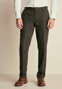 Pantalones ajustados de color gris oscuro con una textura suave, que presentan un frente plano y pliegues, combinados con zapatos brogue marrones.