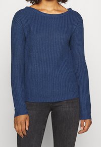 Pull en tricot bleu avec un large col côtelé, des manches longues et un motif texturé. Fini par un ourlet côtelé à la taille et aux poignets.