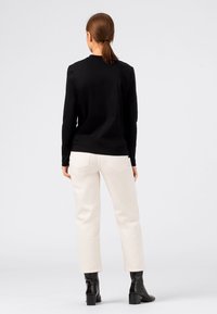 Musta pitkähihainen yläosa, istuva ja pyöreällä kaula-aukolla; yhdistetty kermanvärisiin, lyhytlahkeisiin housuihin; asun täydentävät mustat nilkkurit.