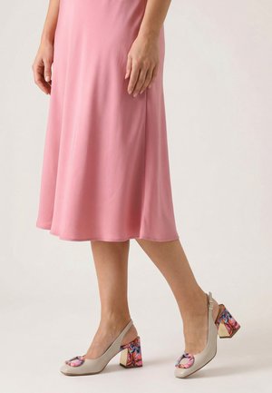 Vrouw draagt een roze midi-rok en beige slingback blokhakken met een meerkleurig bloemenpatroon op de hakken en gespen.