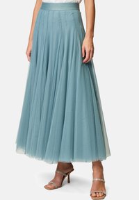 A flowing, light blue tulle skirt with a fitted waistband, featuring vertical pleats and a long, layered design, paired with strappy heels.