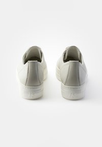 Baskets en cuir blanc avec une texture lisse, semelles en caoutchouc blanc plates et un onglet de talon en boucle. Présente un détail de logo subtil au niveau du talon.