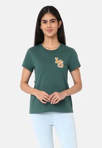 T-shirt en coton vert à manches courtes, col rond, avec un logo brodé "LS" en orange et jaune sur le côté gauche de la poitrine.