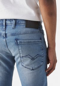 Ljust blå denimjeans med en texturerad yta, bakficka med zigzag-stygn och en svart läderpatch med varumärket.