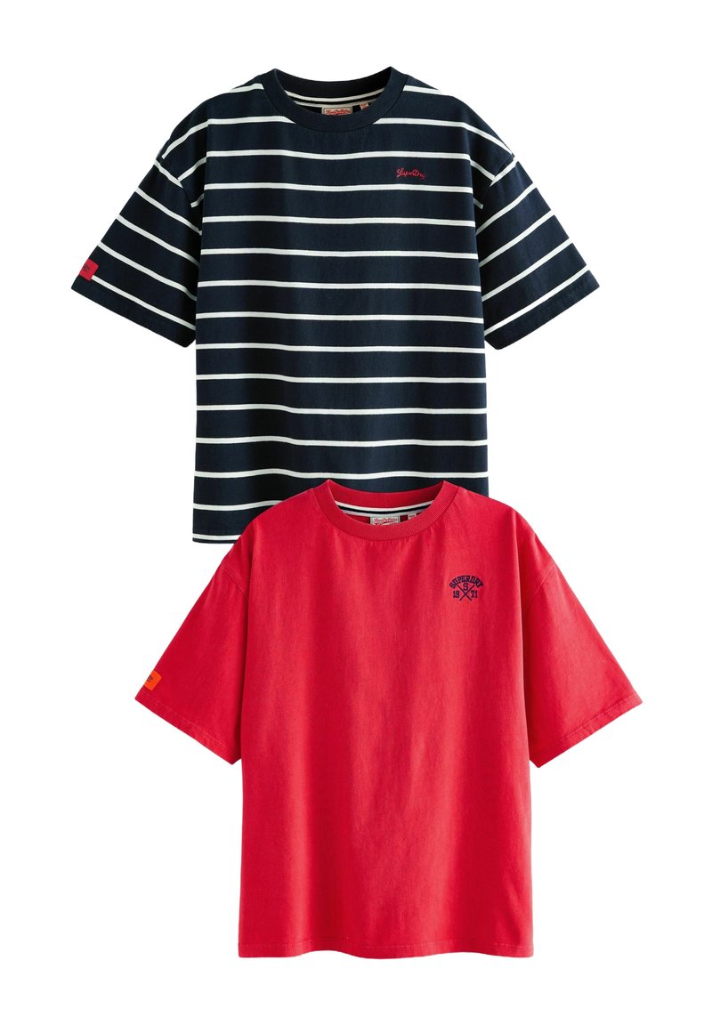 Zwei T-Shirts: eines in Marineblau mit weißen Streifen und rotem Logo; das andere ein einfarbiges Rot mit kleinem blauen Logo. Beide haben kurze Ärmel und runde Ausschnitte.