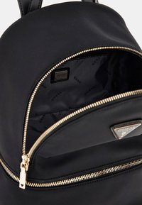Zaino in nylon nero con zip dorata, placca con logo e interno foderato con un motivo a ripetizione del nome del marchio. Design con parte superiore arrotondata.