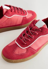 Rote Sneakers aus Wildleder und synthetischen Materialien, mit einem weißen Akzent, strukturierten Einsätzen, runden Schnürsenkeln und einer Sohle aus Gummi.