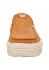 Tan suede slip-on shoe with ribbed beige sole and logo patch at the back. Features rounded toe and minimalist design.