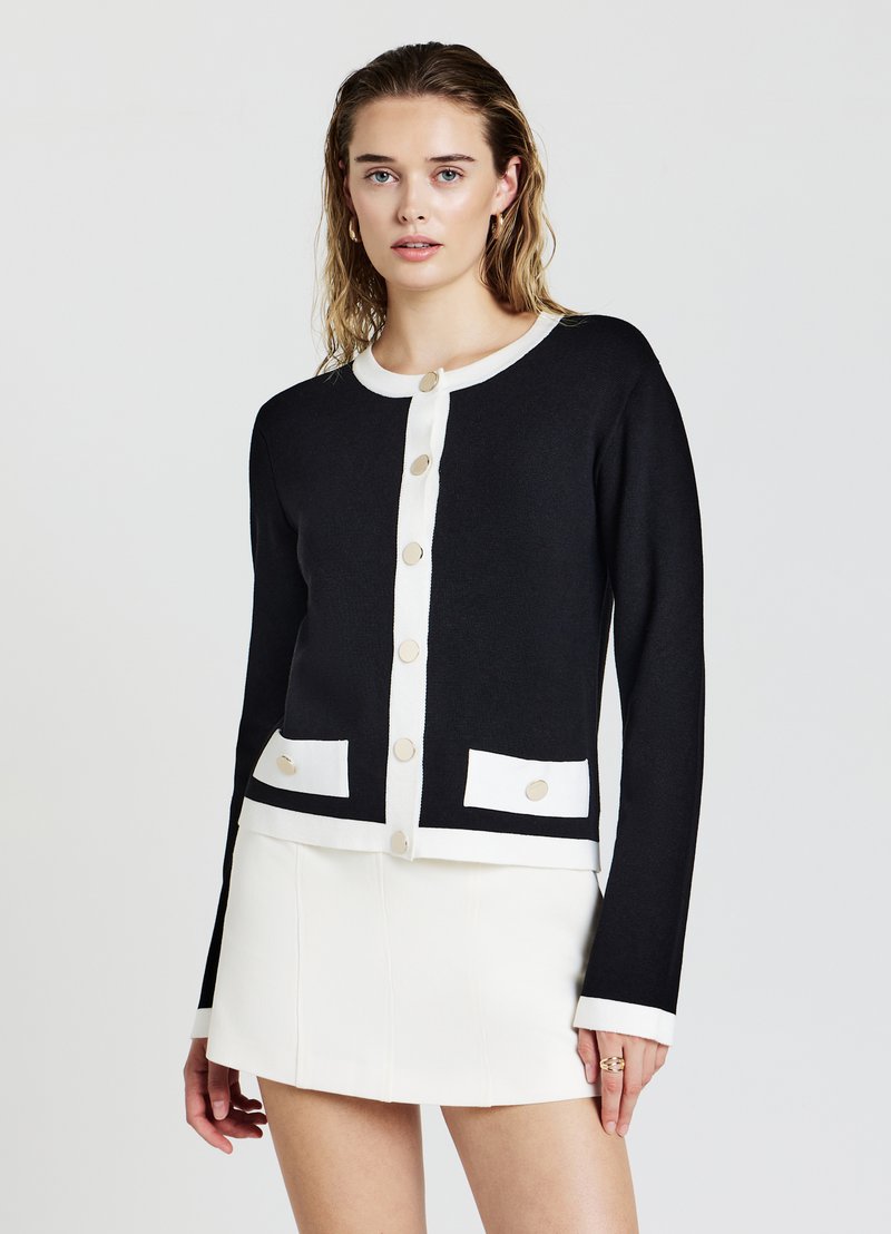 Schwarze Strickjacke mit weißem Besatz, runder Ausschnitt, langen Ärmeln und dekorativen Knöpfen. Mit zwei Fronttaschen.