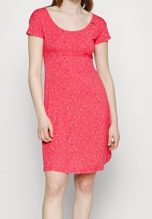 Mujer con vestido rojo de manga corta y largo hasta la rodilla con un pequeño estampado floral blanco y negro sobre un fondo claro y liso.