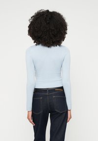 Ανοιχτό μπλε προσαρμοσμένο πουλόβερ με μακριά μανίκια, ραμμένο στρίφωμα, συνδυασμένο με σκούρα μπλε τζιν με πέντε τσέπες και καφέ δερμάτινη λεπτομέρεια.