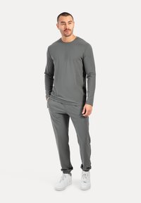 Graues Langarmshirt und dazu passende Hose aus weichem, dehnbarendem Stoff. Das Outfit hat eine lockere Passform und tapered Hosenbeine, kombiniert mit weißen Sneakers.