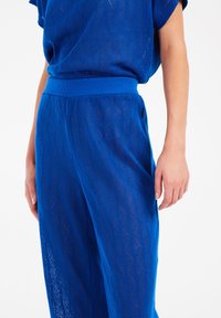 Blauw gebreid loungewear set met een ruitpatroon. Het bovenstuk heeft een losse pasvorm, en de broek heeft een elastische tailleband en zijzakken.