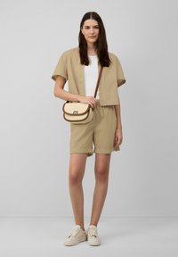 Beige bijpassende set met een kortebloes met knopen en shorts, gecombineerd met een crèmekleurige schoudertas en beige sneakers. Soepele stoffen structuur.