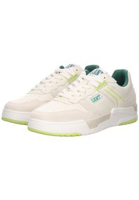 White athletic shoes with green accents and textured panels. Features perforations on the toe, flat laces, and a rubber sole.