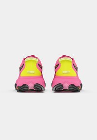 Sportssko med en livlig rosa overdel med gule detaljer, et teksturert design og en svart gummisåle med synlige gripe mønstre.