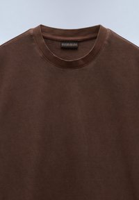 T-shirt marrone a girocollo realizzato in morbido cotone. Presenta una texture liscia e un piccolo etichetta del marchio sul colletto.