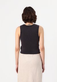 Svart ribbad linne med rund halsringning och ärmlös design, tillsammans med en ljust färgad kjol. Texturerad och figurnära silhuett.