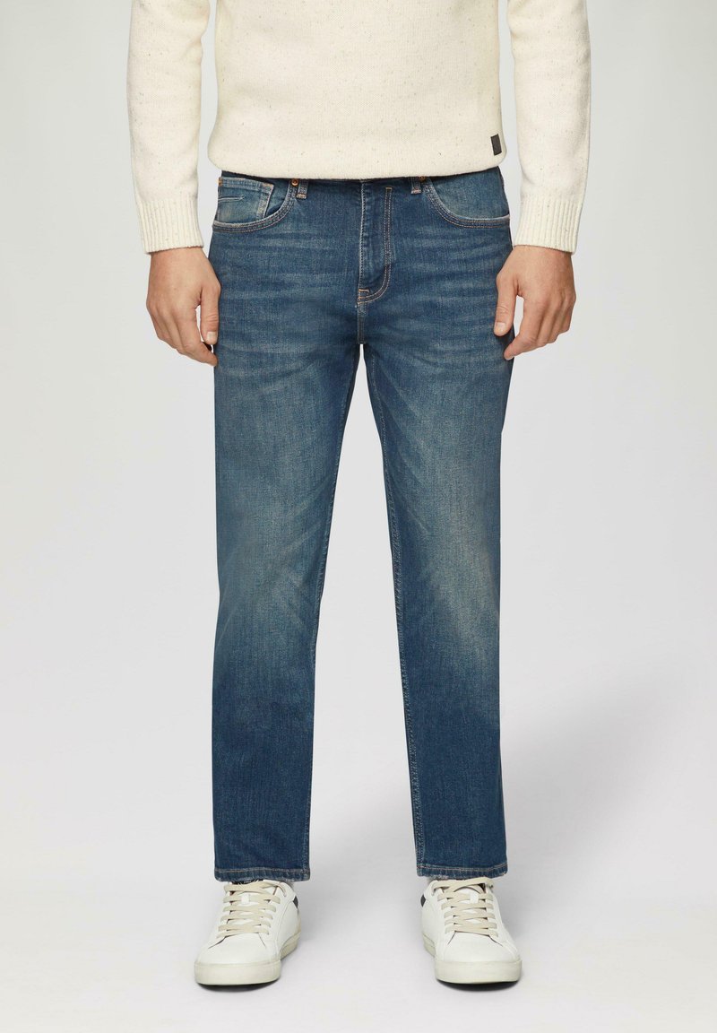Blue denim jeans with a straight leg design, five-pocket style, subtle fading, and contrast stitching, paired with white sneakers.